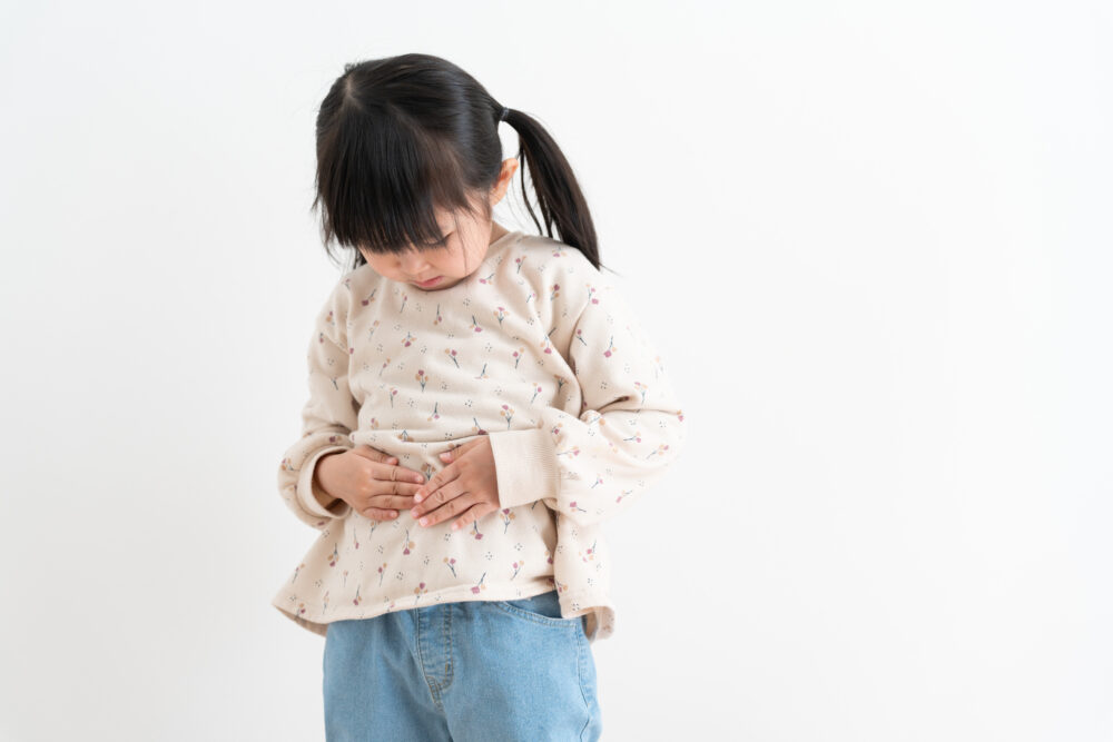 お腹を押さえて不安そうな表情の小学生の女の子